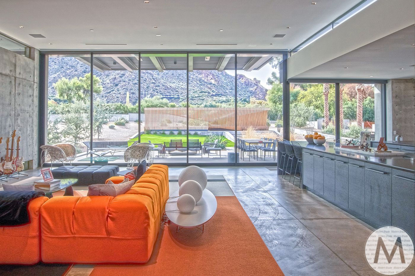 Modern living room with orange couch, large windows overlooking outdoor area, and a mountain view.
