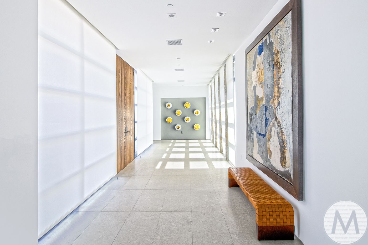 Long hallway with art, bench, and a wooden door, bathed in natural light.