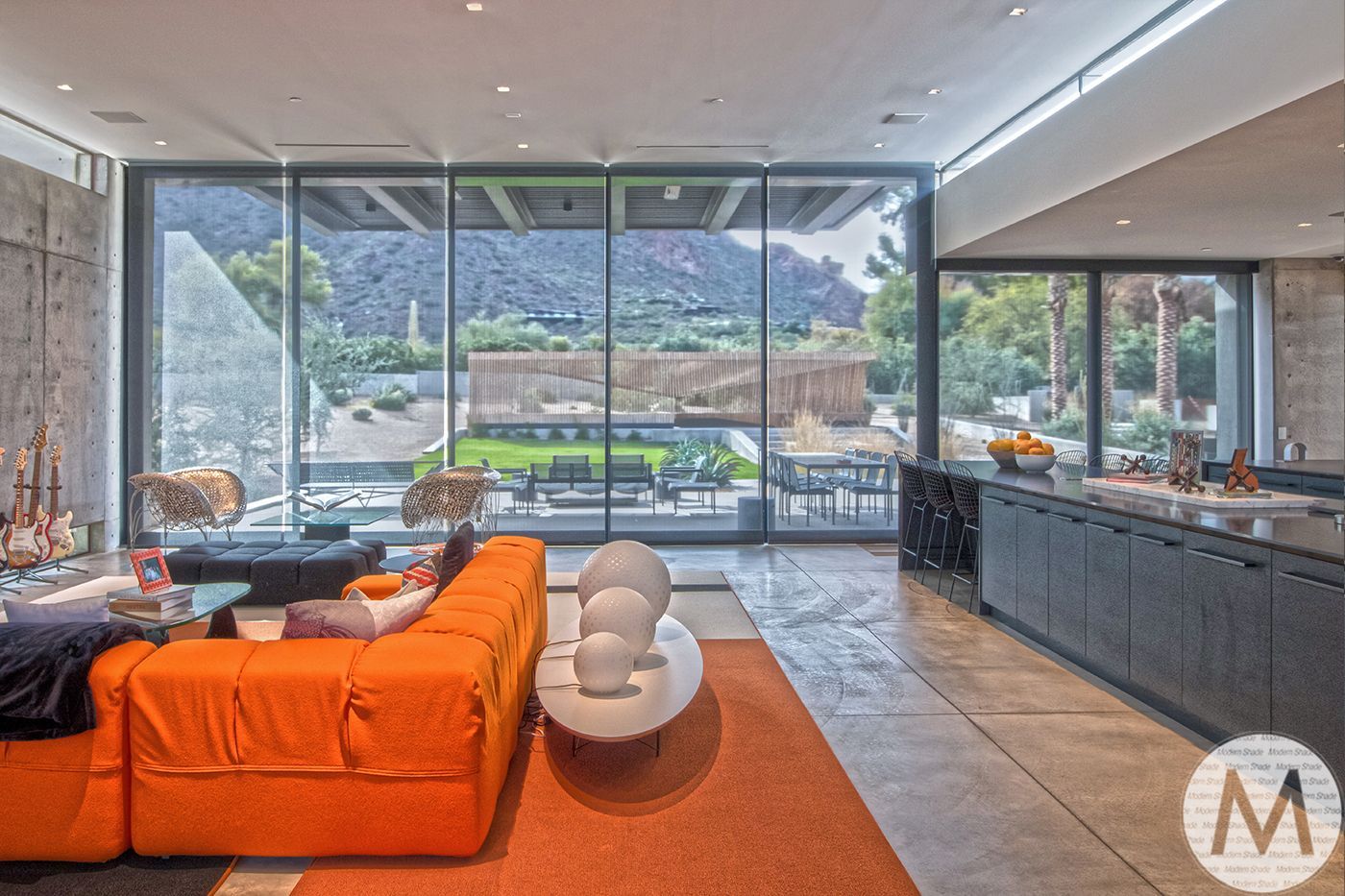 Modern living room with an orange sofa, open to a backyard view and mountains.