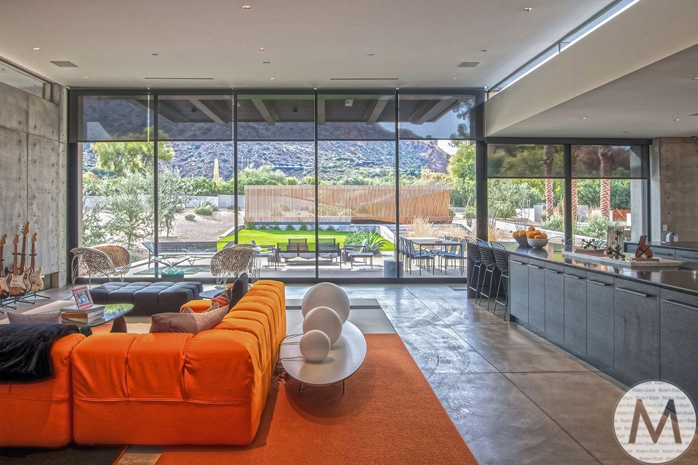 Bright orange sofa in modern living room with large windows overlooking a patio and mountains.