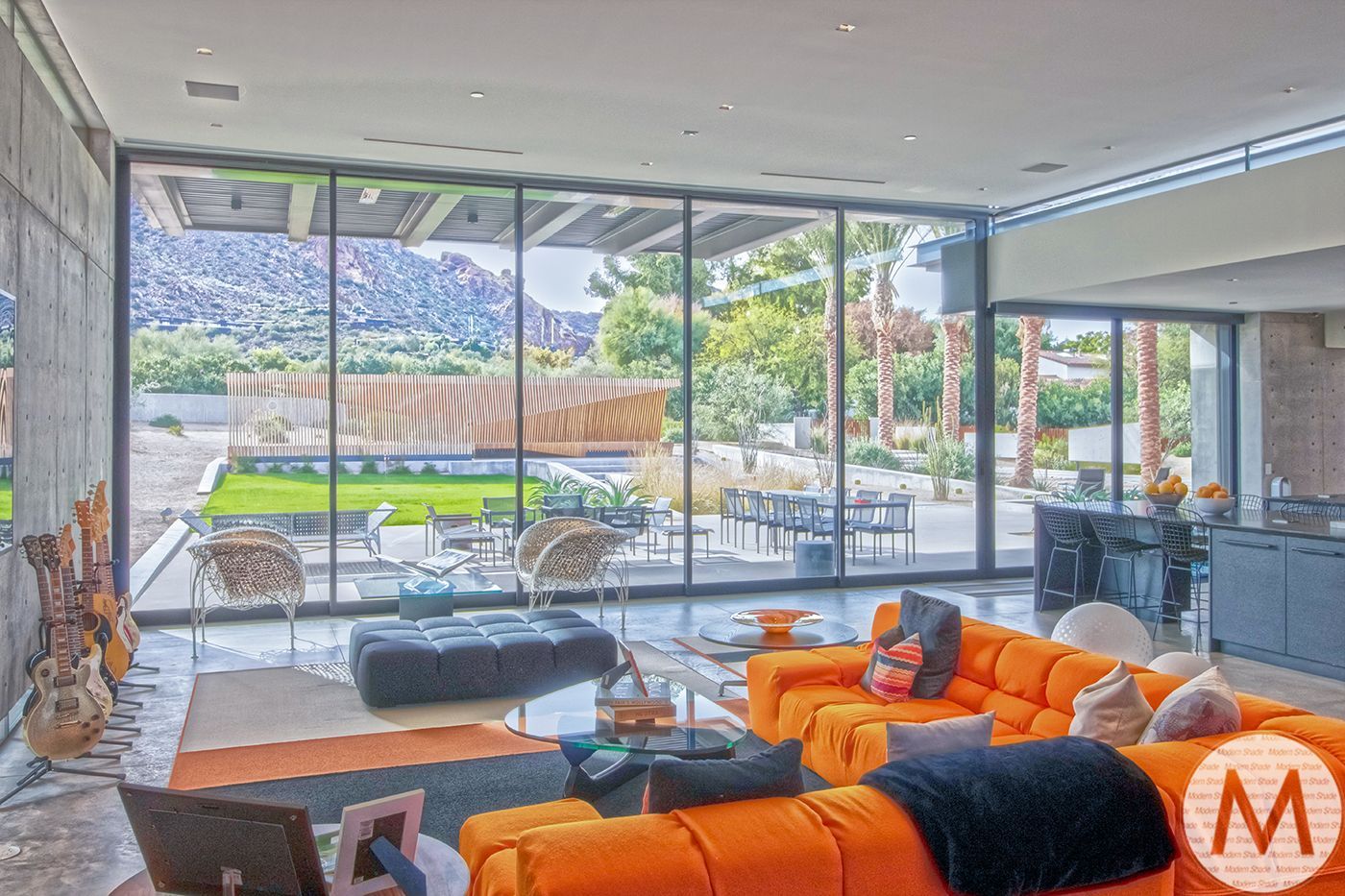 Spacious modern living room with an orange sofa and large windows overlooking a backyard with mountain views.