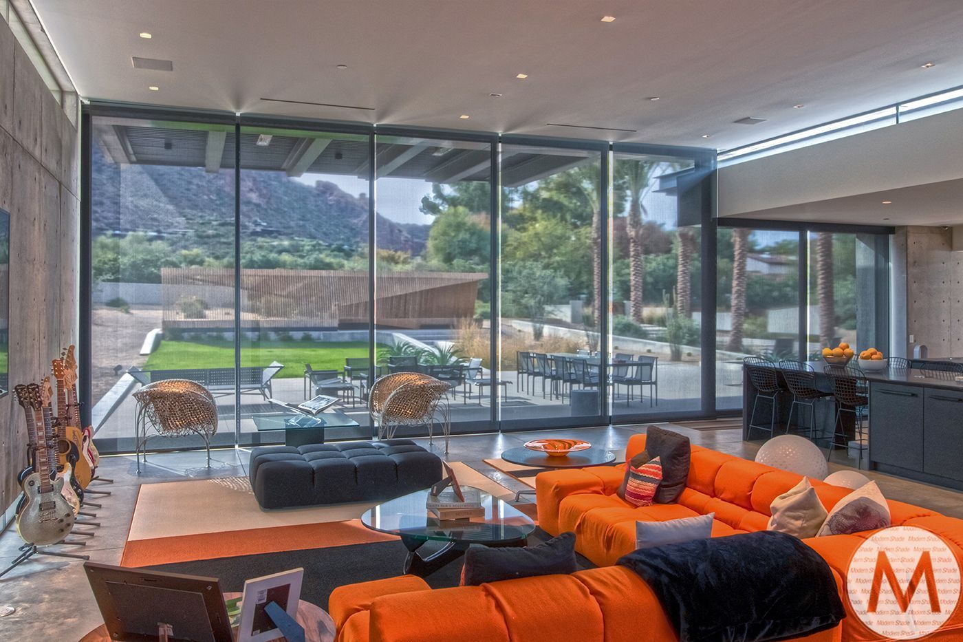 Modern living room with large glass windows, orange sectional, and outdoor view.