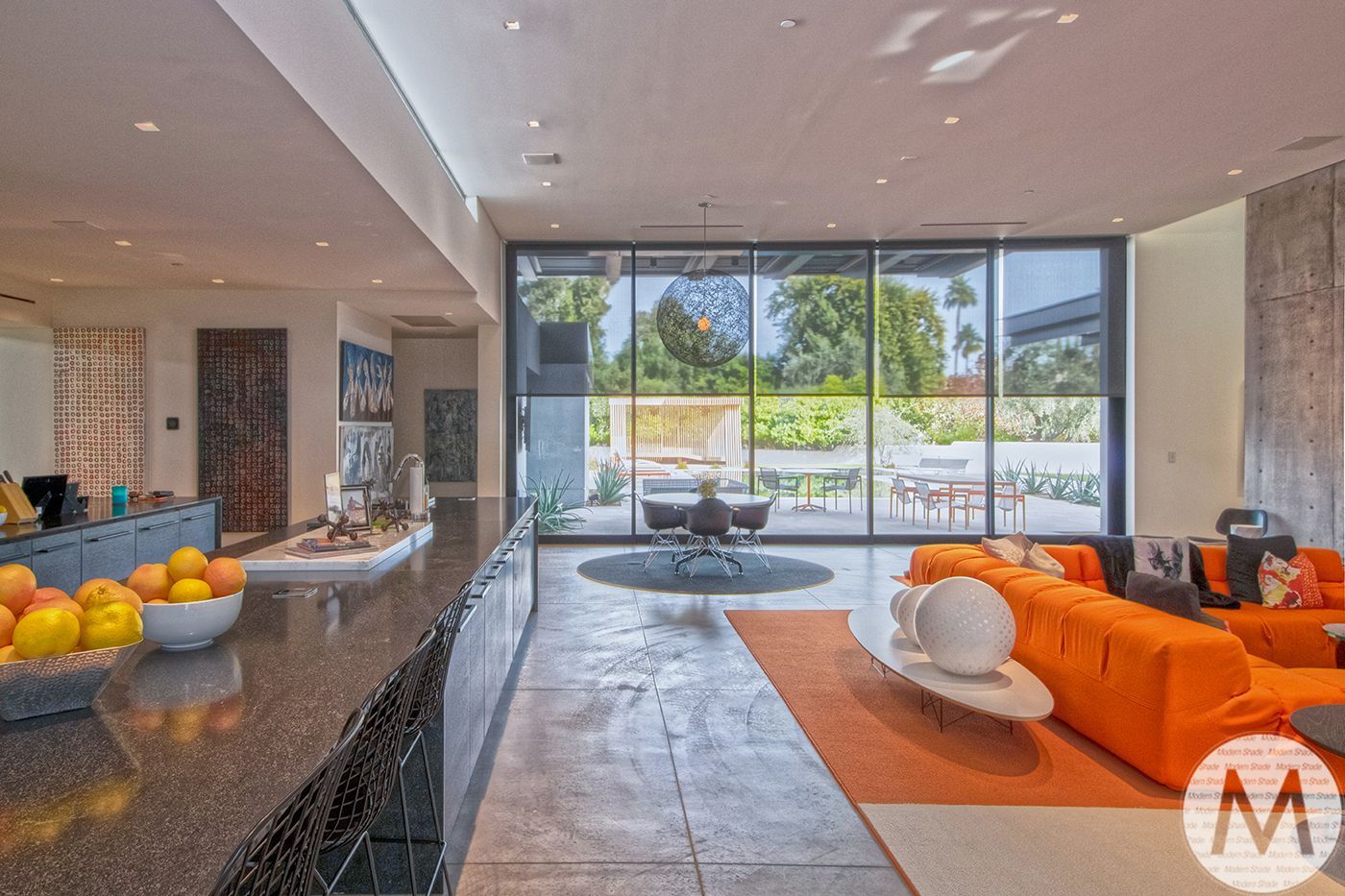 Modern open-plan living room with orange couch, stone bar, and large glass doors overlooking a yard.