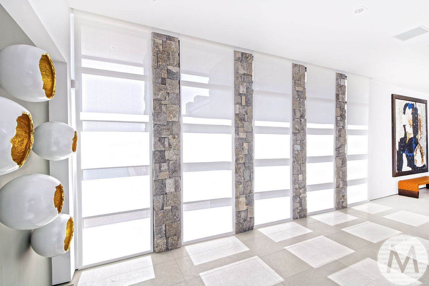Bright room with stone columns and white shades, artwork, and sculptures on the wall.