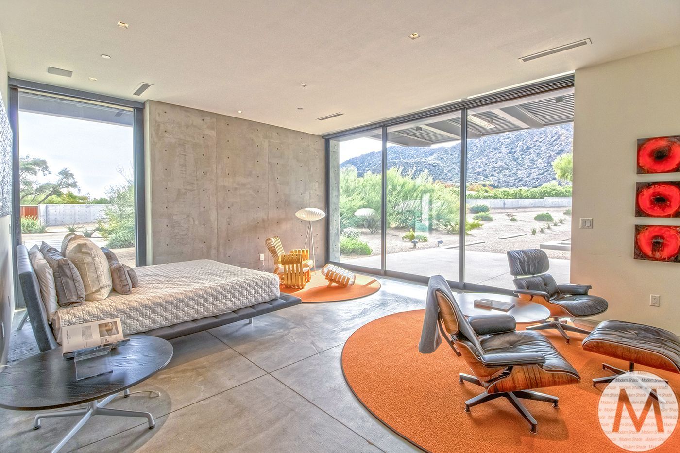 Modern living room with concrete walls, large windows, and orange rugs.