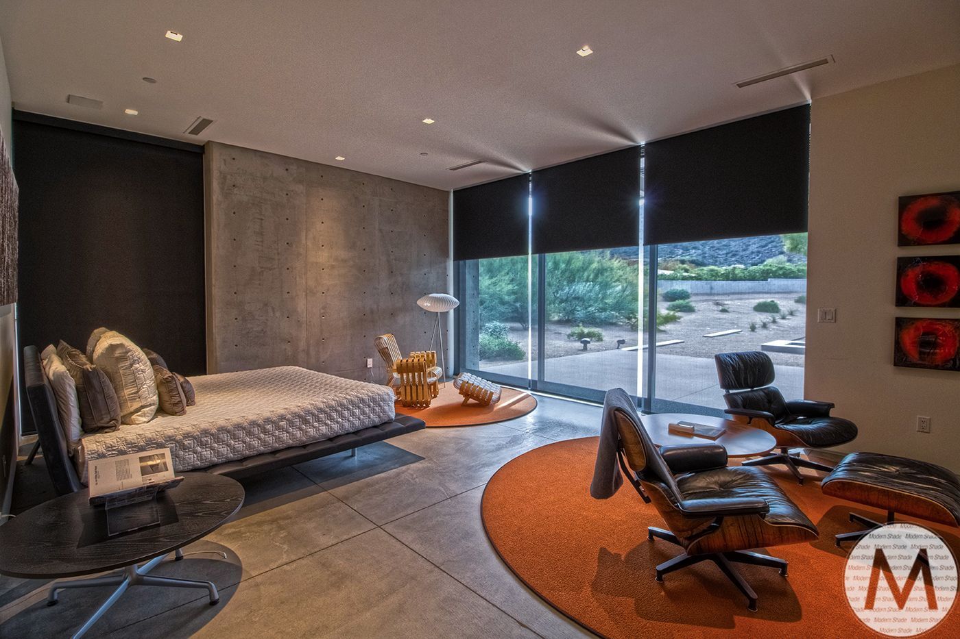 Modern bedroom with a bed, chairs, and a large window overlooking a desert landscape. Orange rug and accents.