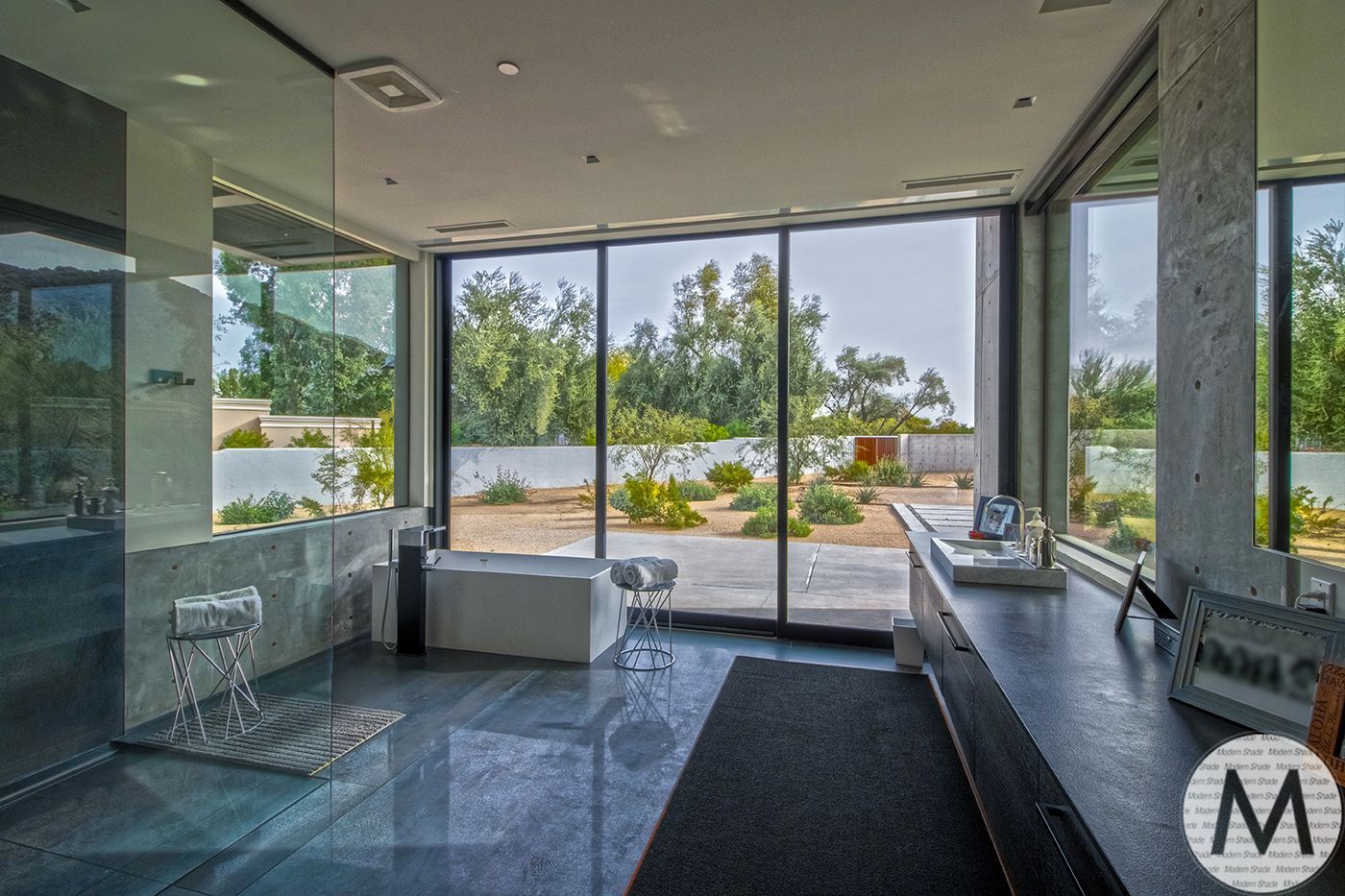 Modern bathroom with large windows, stone floor, white tub, and black vanity.