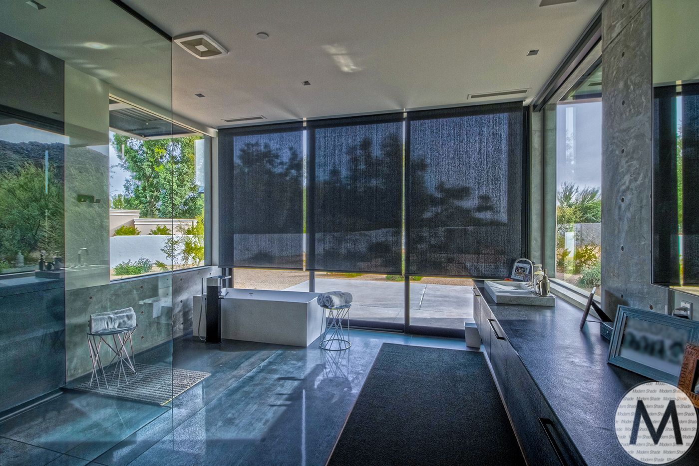 Modern bathroom with dark blinds, open shower, and a view of trees.