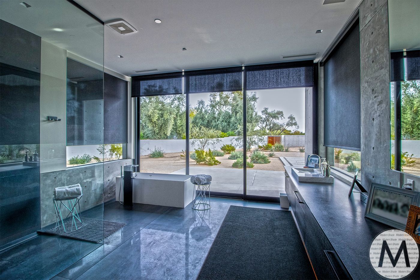 Modern bathroom with large windows, grey tile, and a view of a desert landscape.