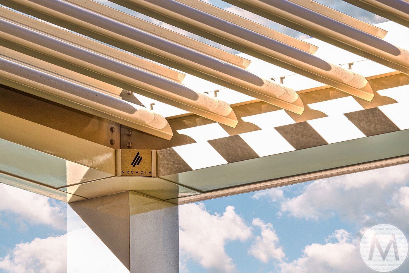 Pergola with angled slats, casting striped shadows on a blue sky.