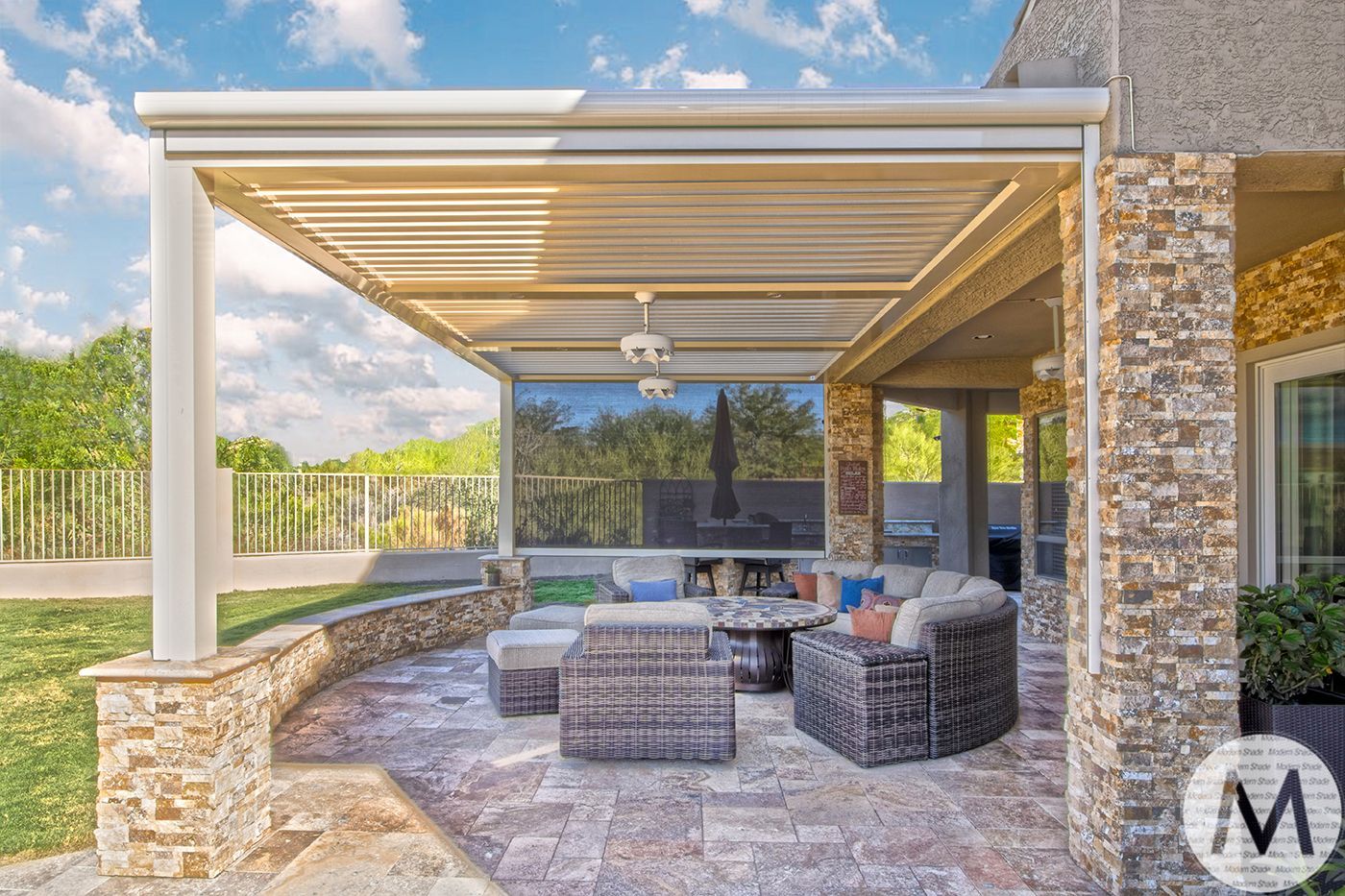 Patio with a pergola, seating area, and stone accents, under a bright blue sky.