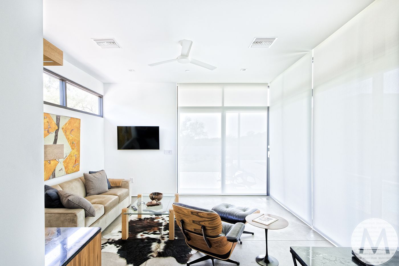 Modern living room with white walls, sofa, art, and large windows.