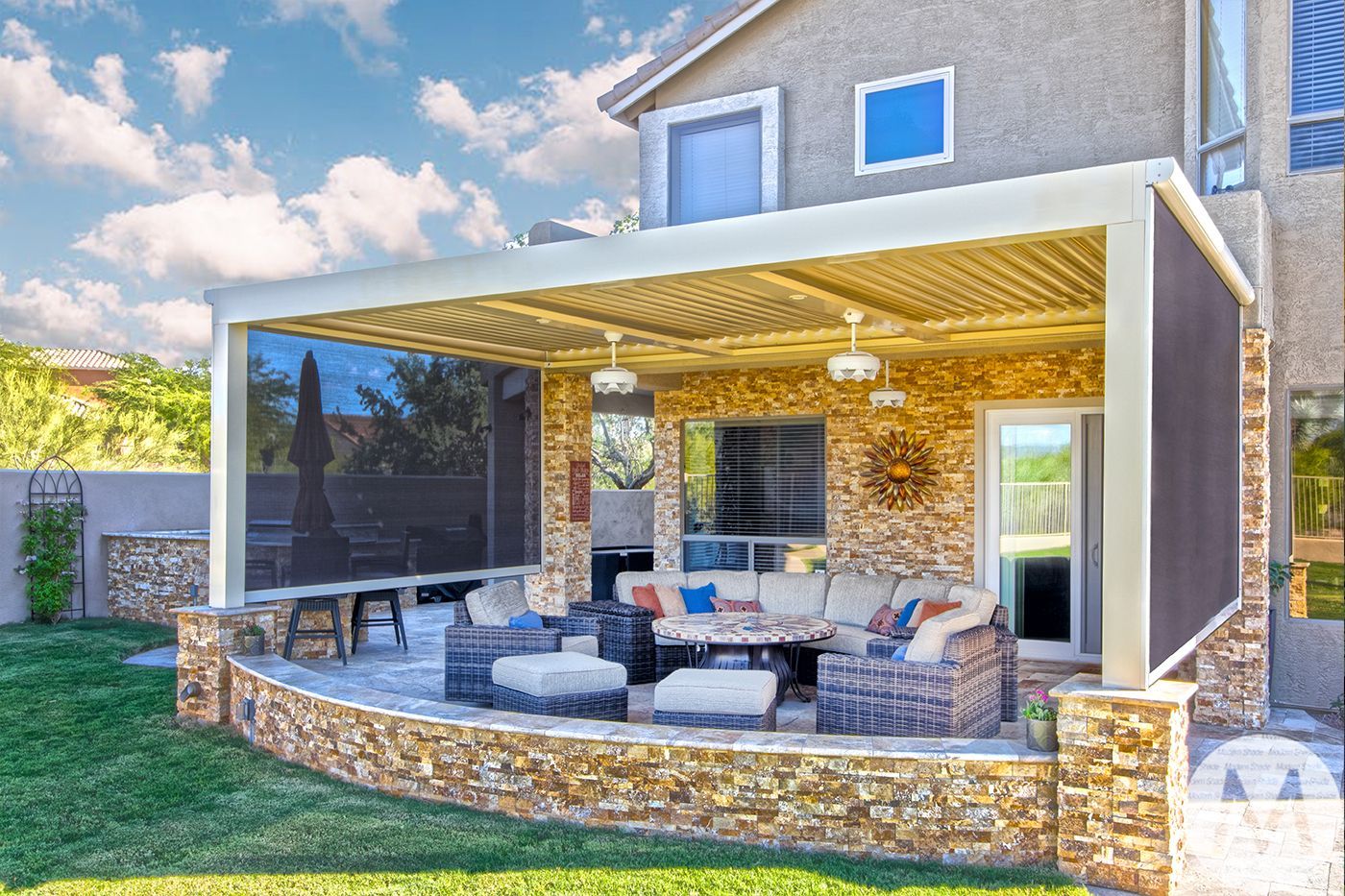 Covered patio with stone accents, outdoor seating, and sun shades.