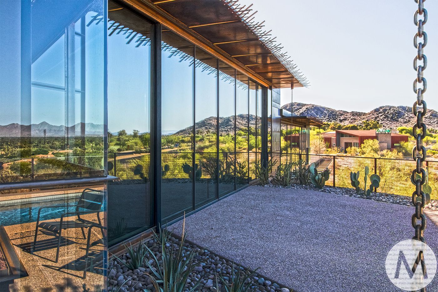 Modern home exterior with floor-to-ceiling windows, gravel patio, and desert mountain view.