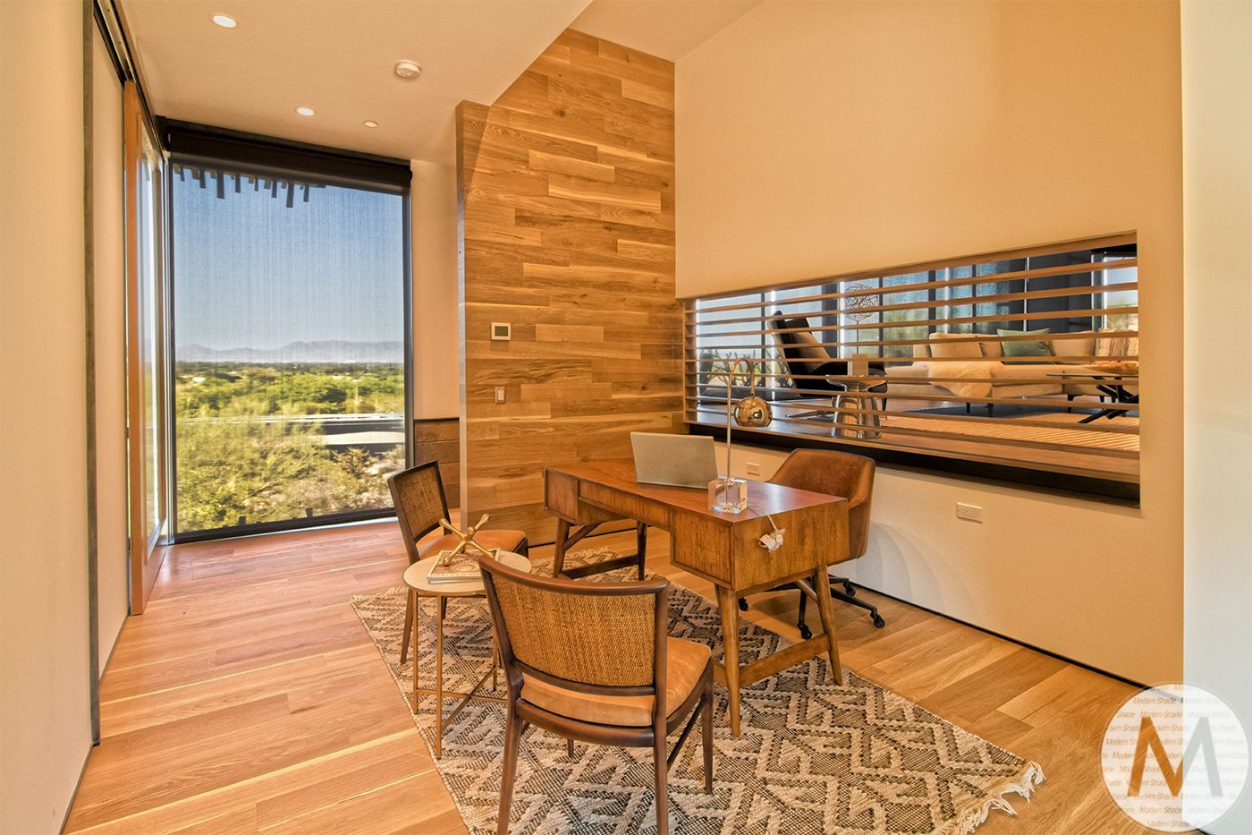 A modern home office with desk, chairs, rug, window with a view, and wood paneling.