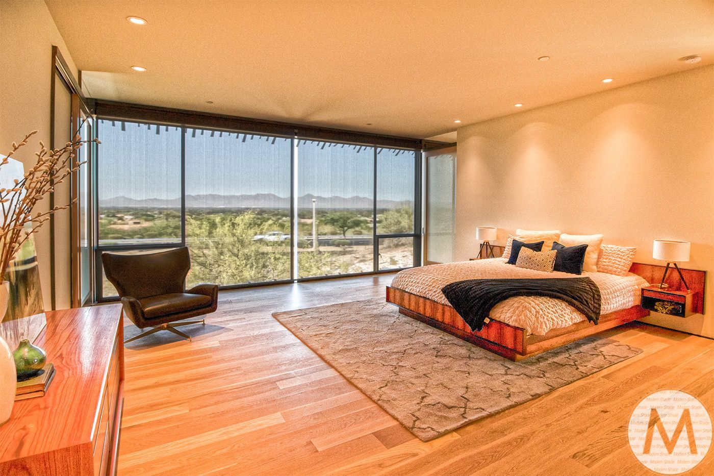 Spacious modern bedroom with large window overlooking a landscape. Features wooden floors, bed, chair, and dresser.