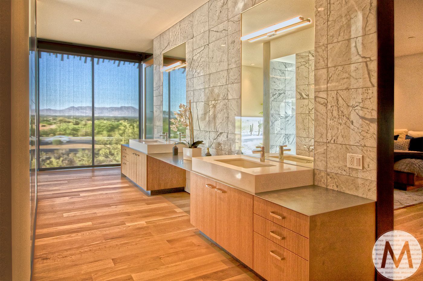 Modern bathroom with wooden floors, stone walls, double sinks, large window with view.