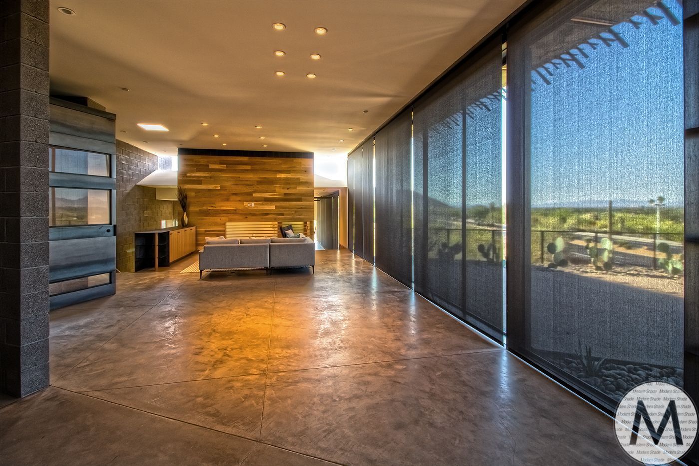 Spacious modern living room with large windows, concrete floor, and a wood-paneled wall.