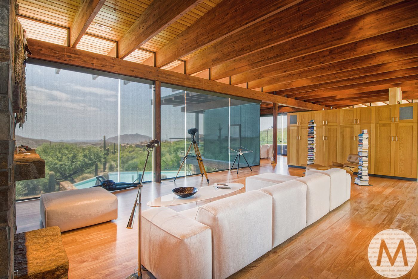 Modern interior with white sofa, floor-to-ceiling windows, wooden beams, and scenic view.