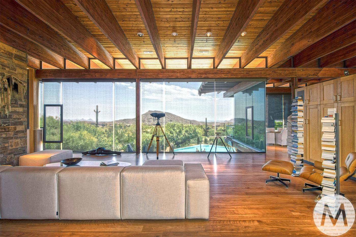 Modern living room with large windows, mountain view, wooden beams, and a beige sofa.