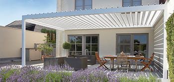 A white pergola covers a patio with a table and chairs. Lavender blooms in the foreground.