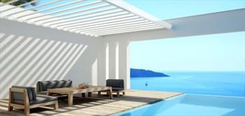 Patio with pool overlooking ocean. White walls, wooden furniture, and blue water.
