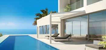 Luxury villa with pool overlooking the ocean; blue sky, palm tree. Two loungers, minimalist design.