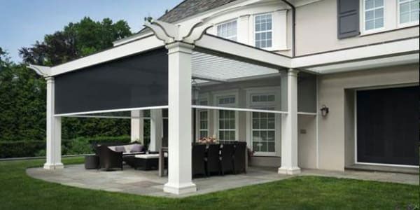 A patio with a black awning and clear side panels attached to a white pergola.