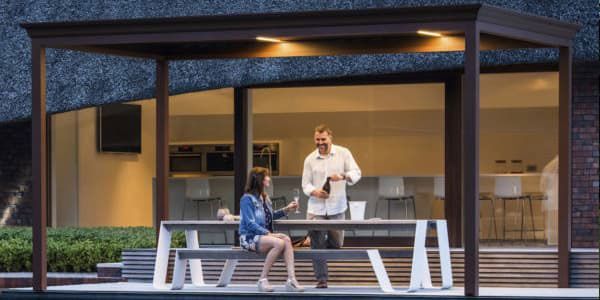 Couple under a pergola at night. Man opening a bottle as the woman sits on bench.