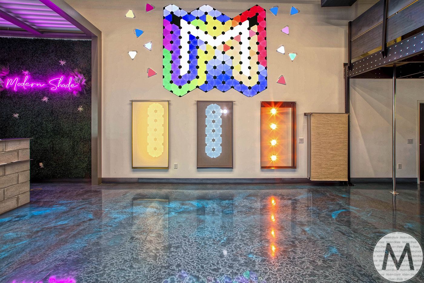 An art gallery with a colorful logo and multiple art pieces on the wall. Shiny, textured floor.