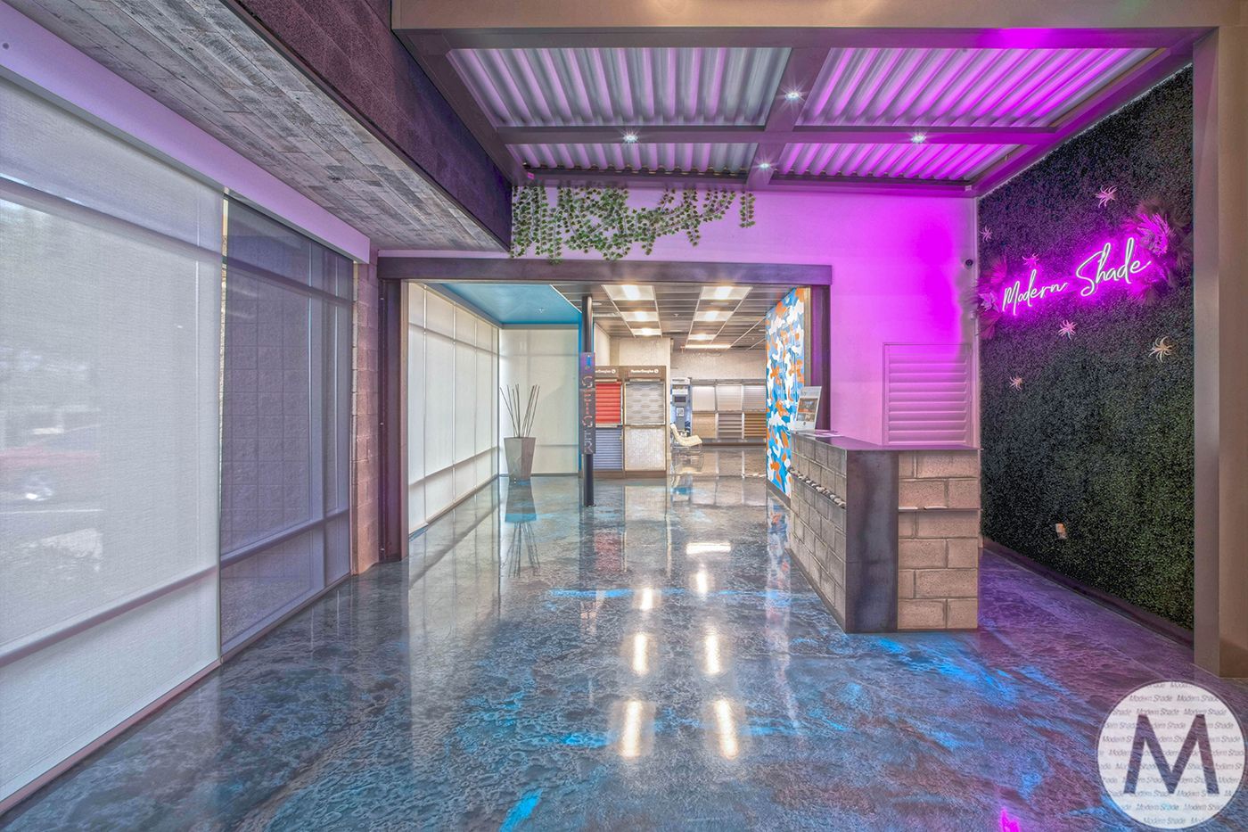 Entrance hall with neon pink light and lush greenery. Polished floor and stone reception desk.