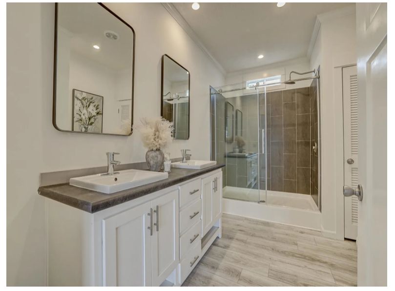 Bathroom with white cabinets, gray countertop, two mirrors, and glass shower.