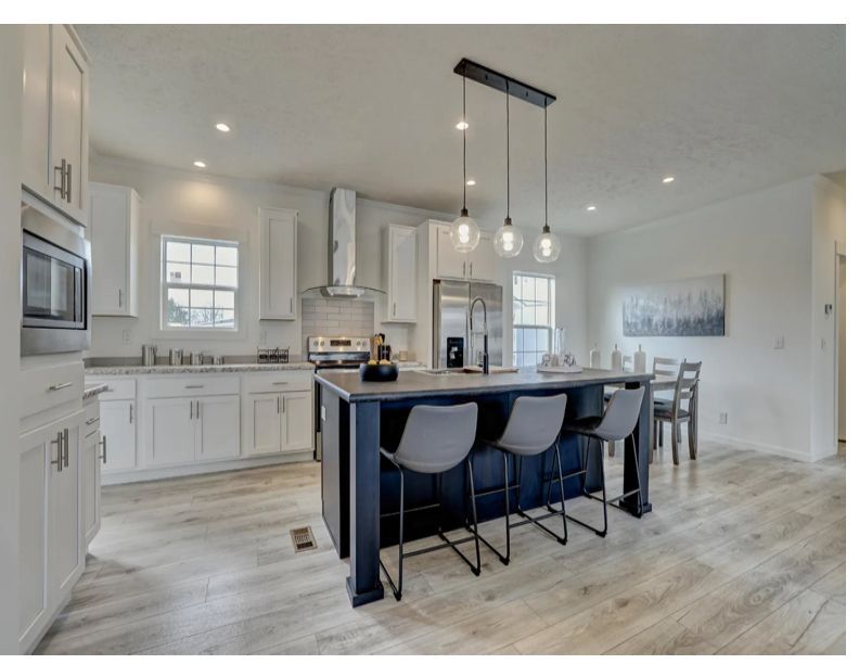 Modern kitchen with white cabinets, navy island, stainless steel appliances, and wood-look flooring.