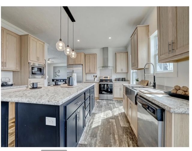 Modern kitchen with wood cabinets, dark blue island, stainless appliances, and pendant lights.
