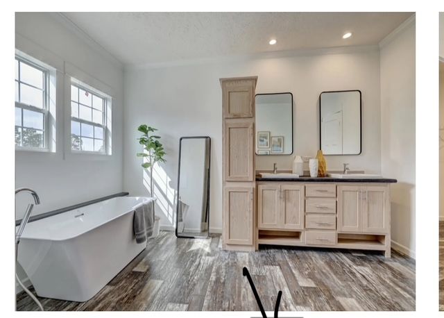 Bathroom with a freestanding tub, double vanity, full-length mirror, and wooden-look flooring. White walls, windows.