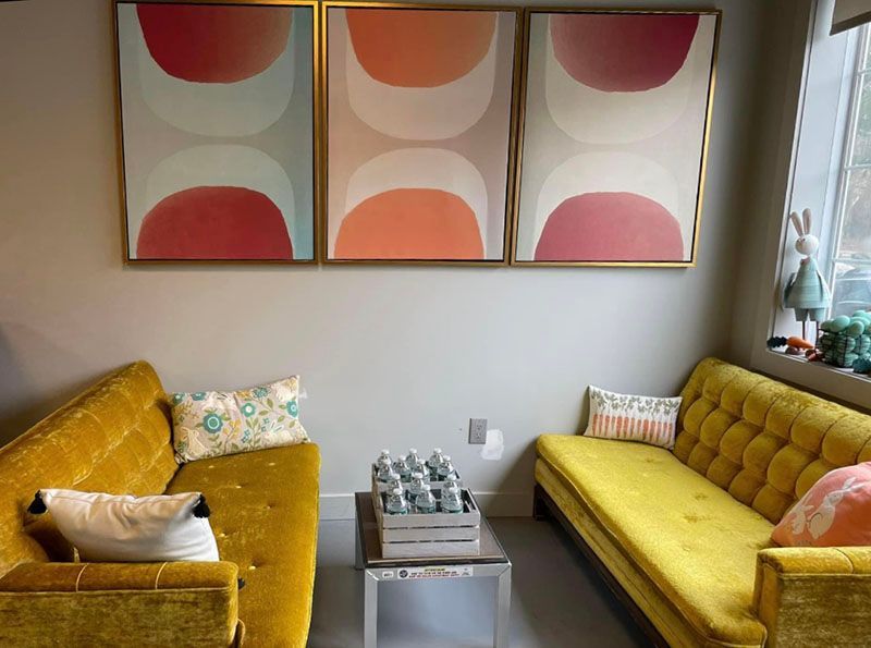 Yellow couches face each other, under abstract art with pink and gold tones. A small table sits between the couches.