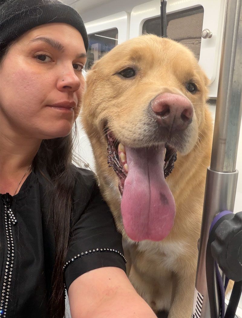Woman and happy yellow dog, both looking at the camera. Dog has tongue out.