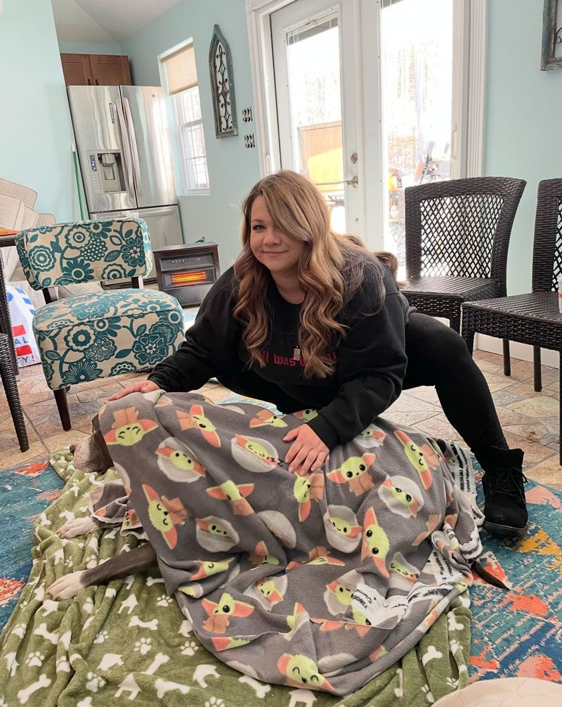 Woman kneels over dog covered with a Star Wars blanket in a living room.