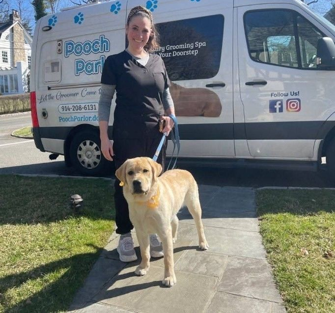 Woman holding a golden retriever puppy at a grooming table. Both are smiling.