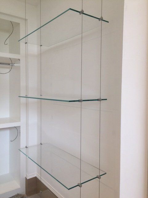 A closet with three clear glass shelves hanging from the wall