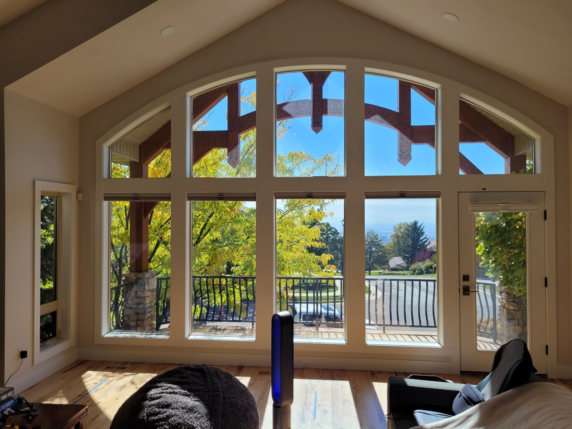 Large arched windows offering a view of trees and sky, with a deck visible outside. Sunlight streams into a room with hardwood floors.