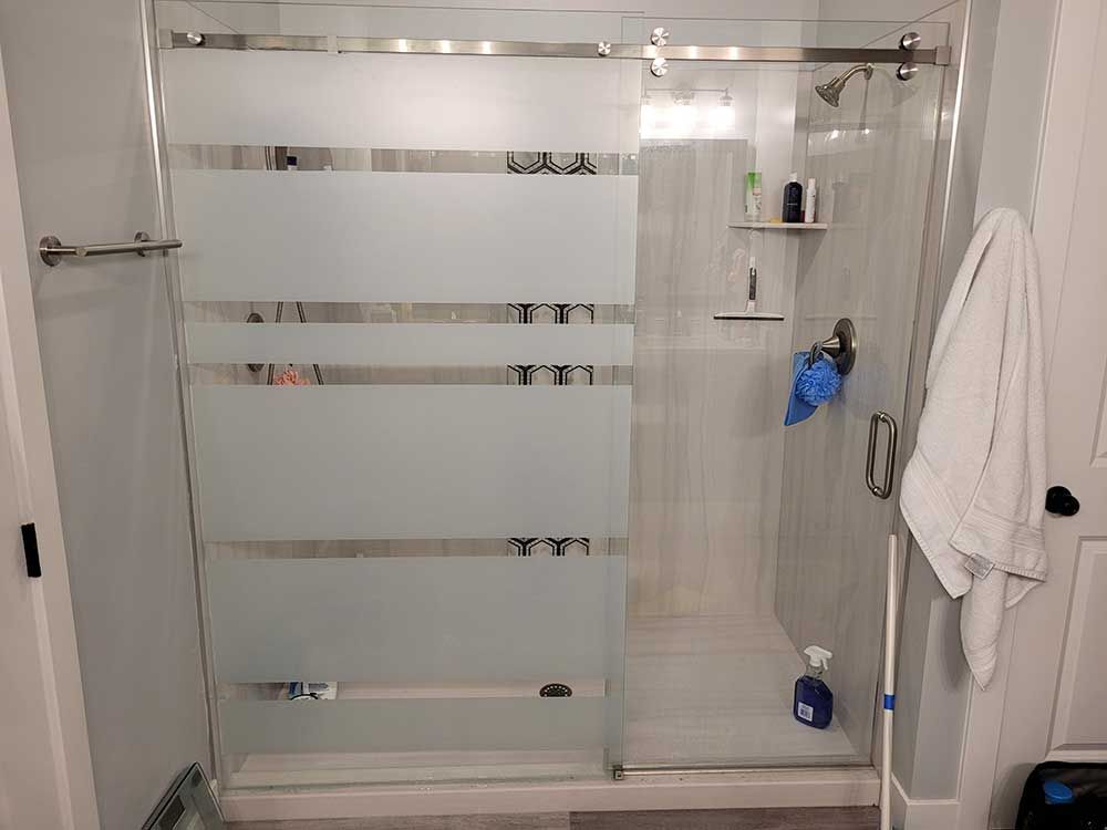 A glass shower with frosted horizontal stripes. A towel hangs on the door and toiletries are visible inside.