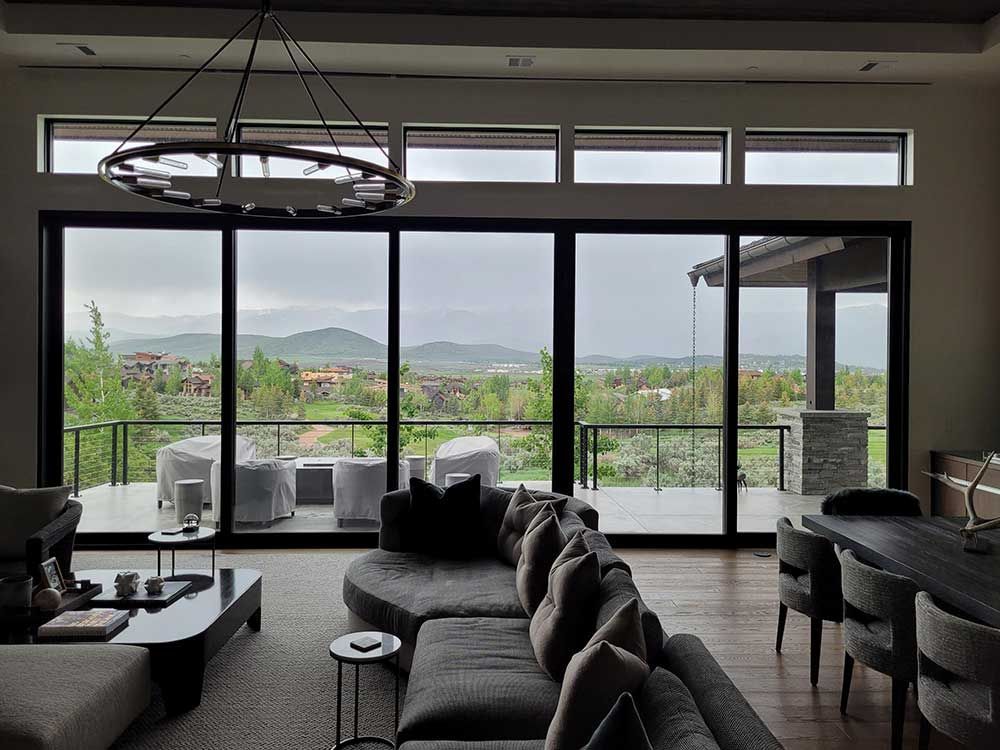 Living room with large glass doors offering a view of a valley. A gray sectional sofa and a dark wood dining table are visible.