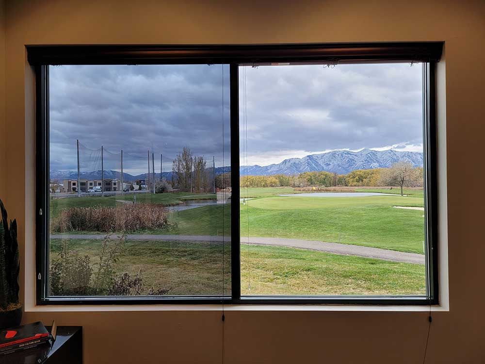A window split in two showing a view. One side is shaded, showing a cloudy day over a golf course. The other is bright.