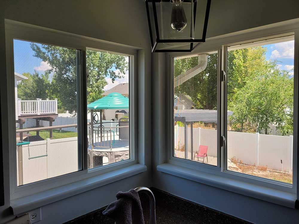 Corner windows overlooking a backyard with a patio, green umbrella, and white fence. A light fixture hangs above.