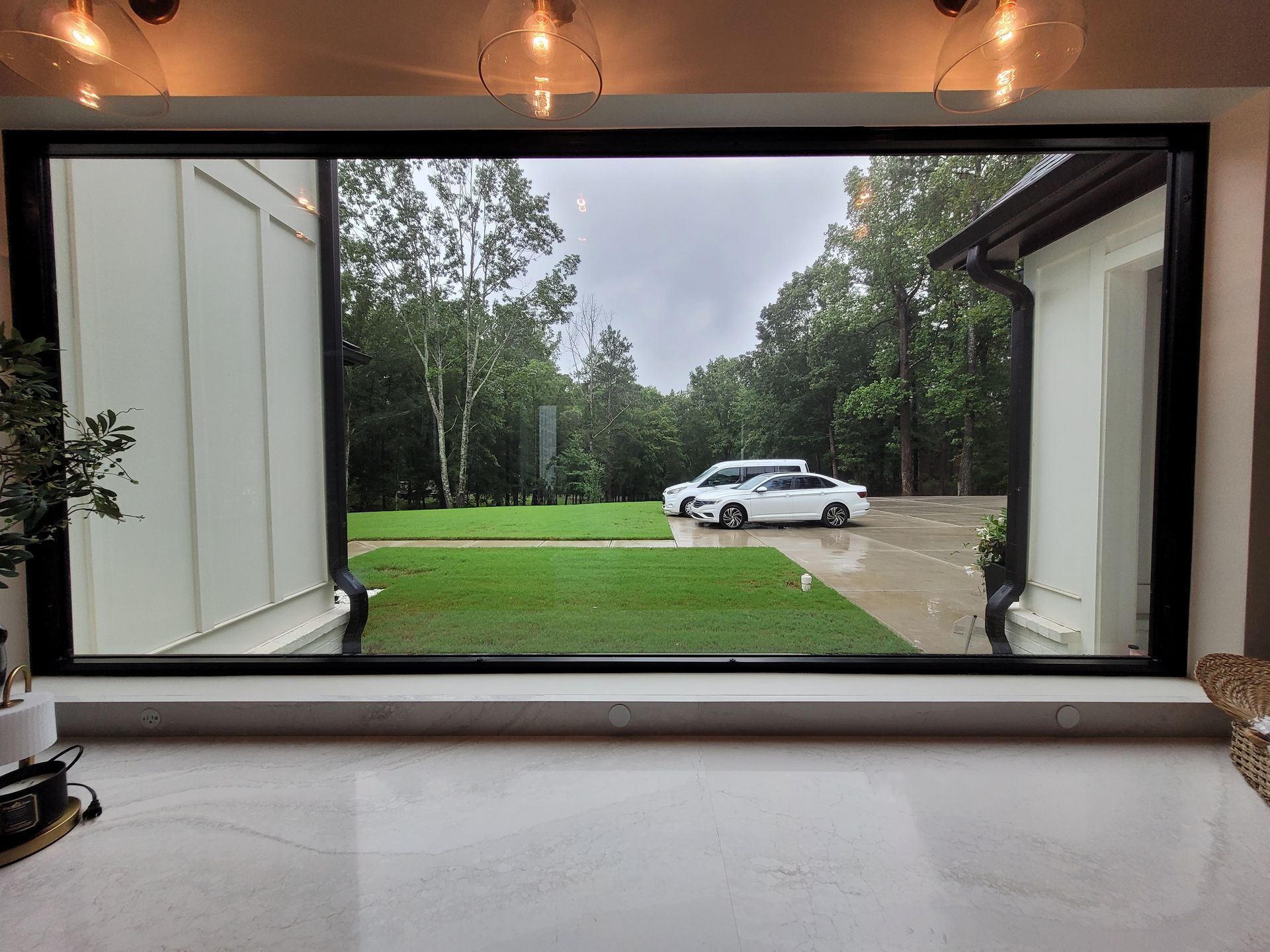 White house exterior with large dark-framed windows reflecting the sky and surrounding buildings; mountain in the background.