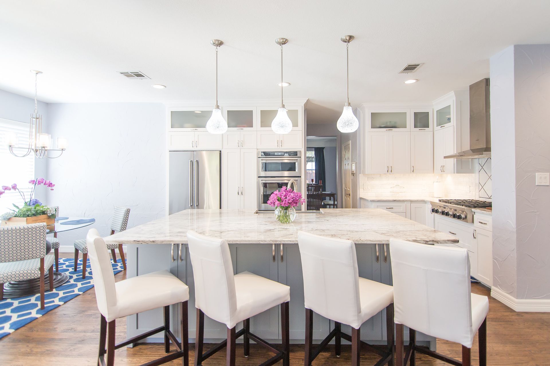 Spacious white kitchen with island, four bar stools, stainless steel appliances, and pendant lights. - After
