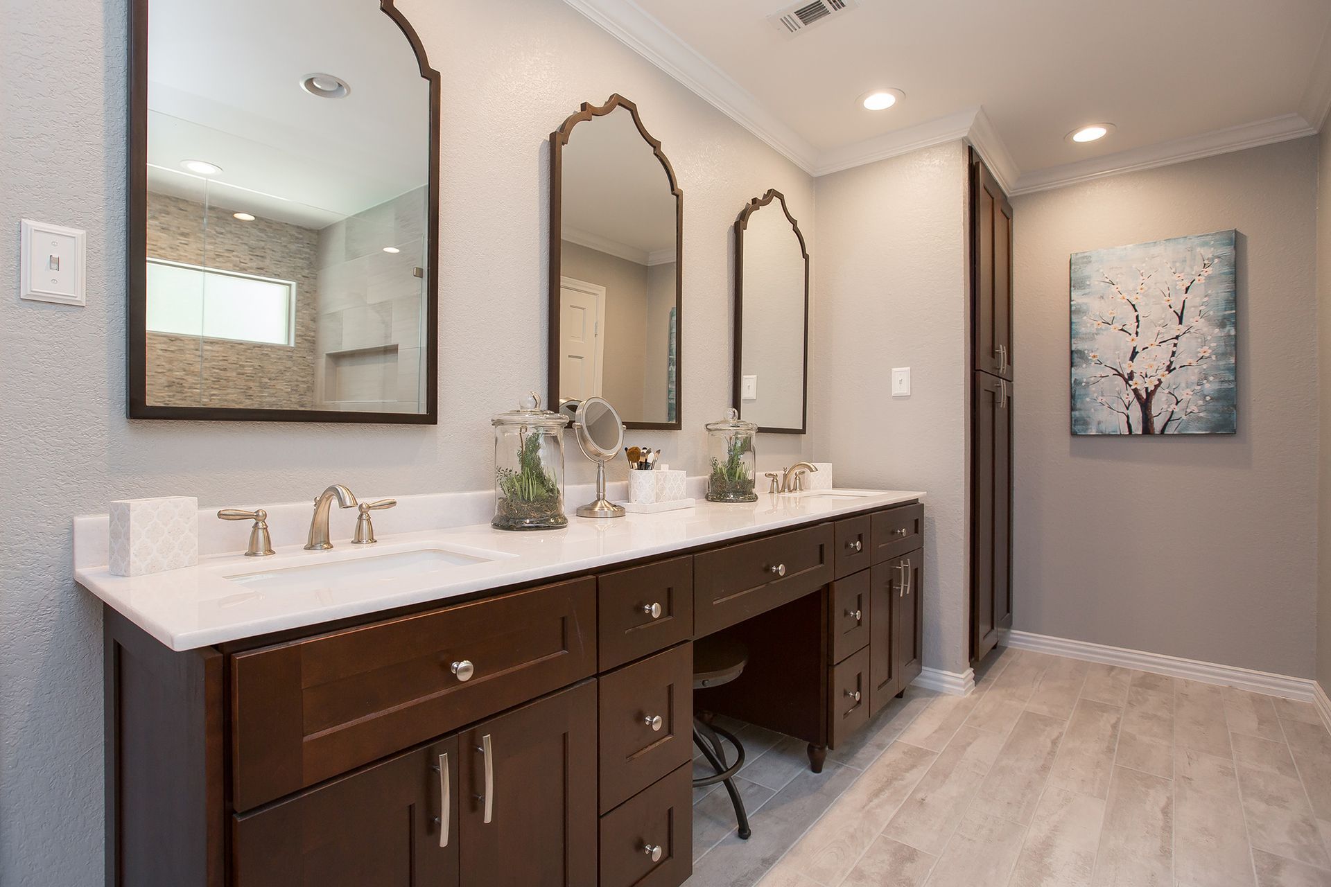 Bathroom with dark wood vanity, white countertops, arched mirrors, and a floral painting.