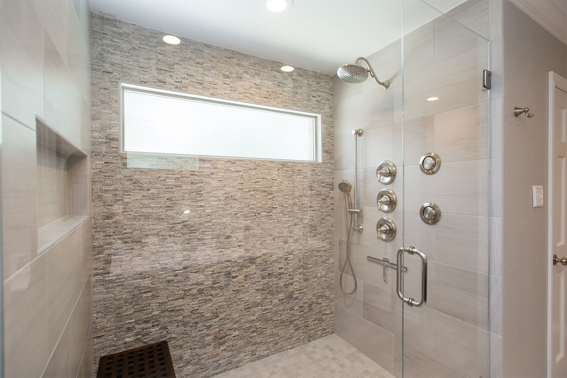 Modern shower with pebble-tiled wall, glass door, multiple water controls, and a window. - After