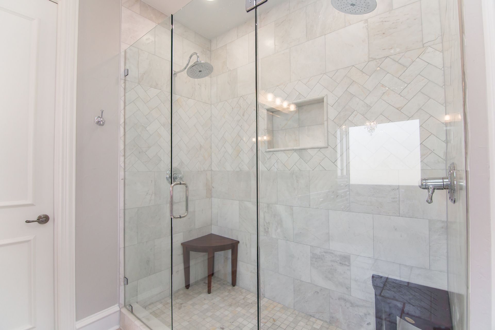 Glass shower with marble tile, a small seat, and chrome fixtures. - After
